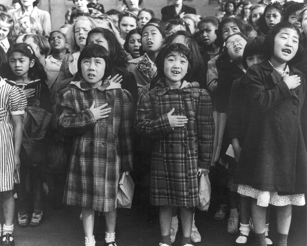A black-and-white photograph of schoolchildren with hands over their hearts reciting the pledge of allegiance in a schoolyard, 1942