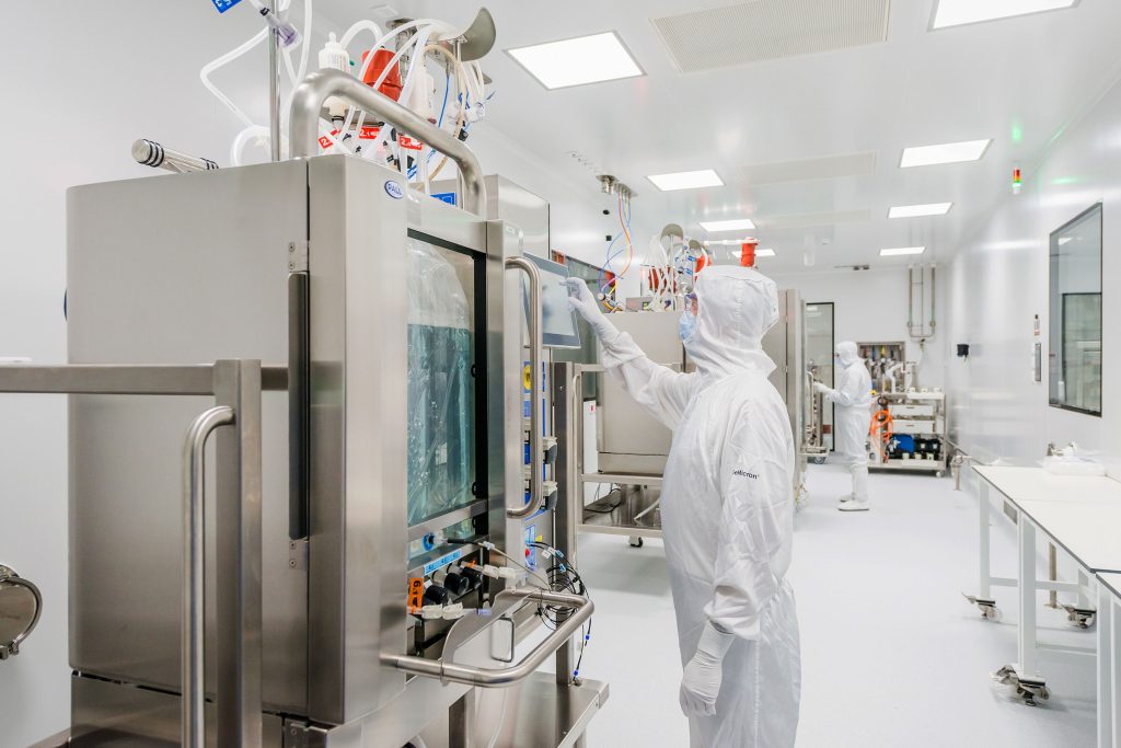 Technician in full cleanroom PPE operating a single-use bioreactor in a brightly lit pharmaceutical manufacturing facility